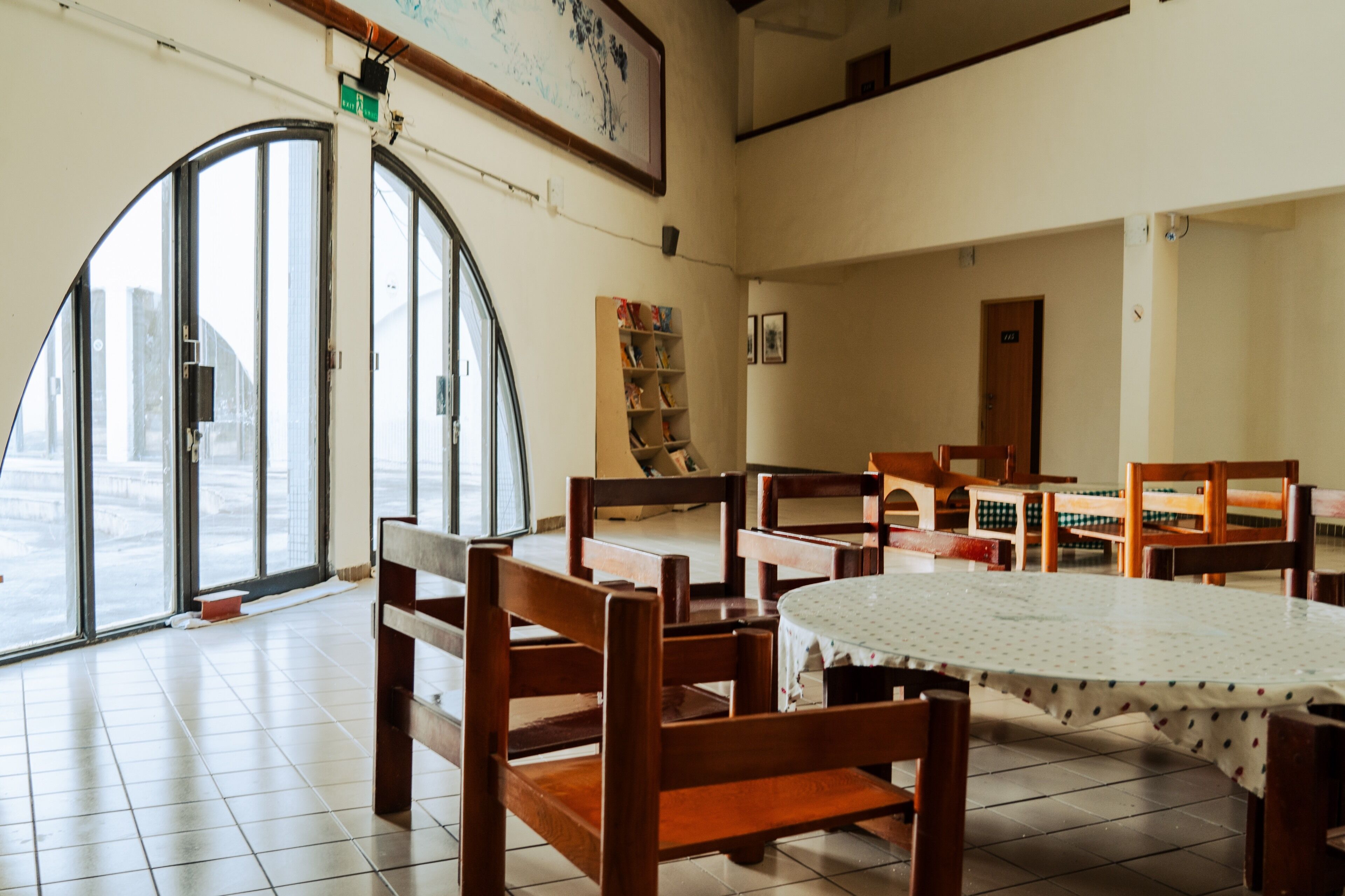 Un comedor con sillas de madera, una mesa redonda, ventanas amplias y una estantería.