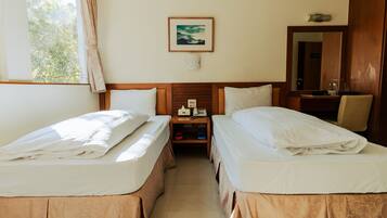 A hotel room with two beds, a nightstand, a mirror, and a window with curtains.