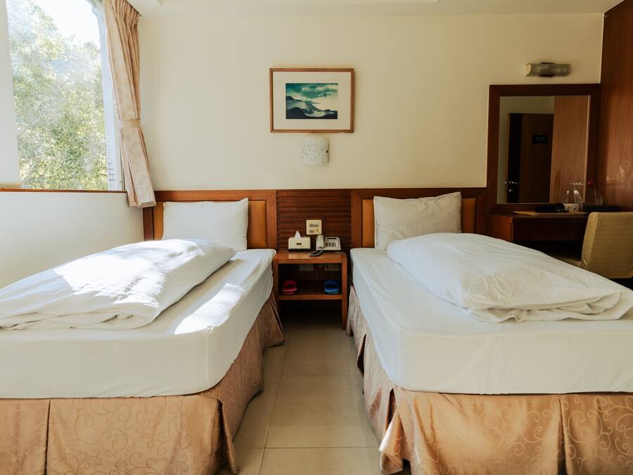 A hotel room with two beds, a nightstand, a mirror, and a window with curtains.
