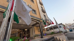 Ingresso di un hotel con bandiere, tra cui una bandiera nazionale, e una facciata con balconi.
