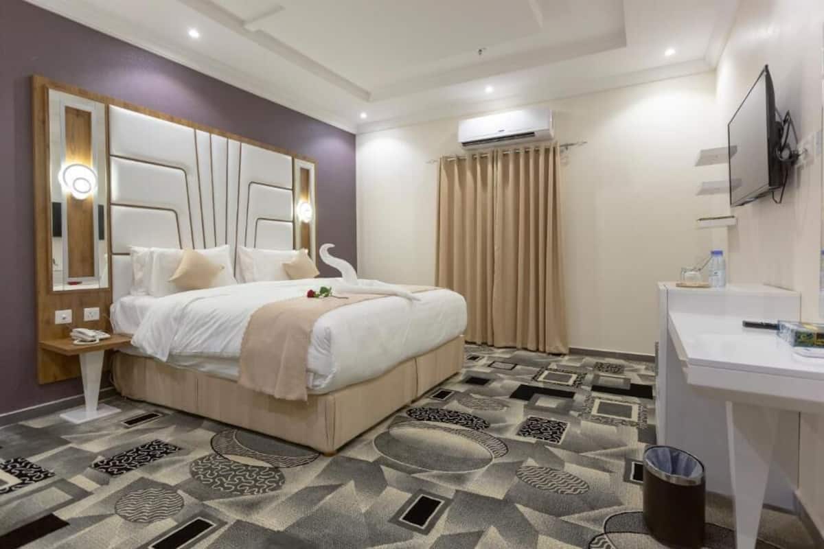 Una habitación de hotel con una cama grande, un escritorio, un televisor y un aire acondicionado.