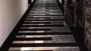 Un lungo e stretto corridoio con pavimento decorato, porte su entrambi i lati e una parete in marmo alla destra.