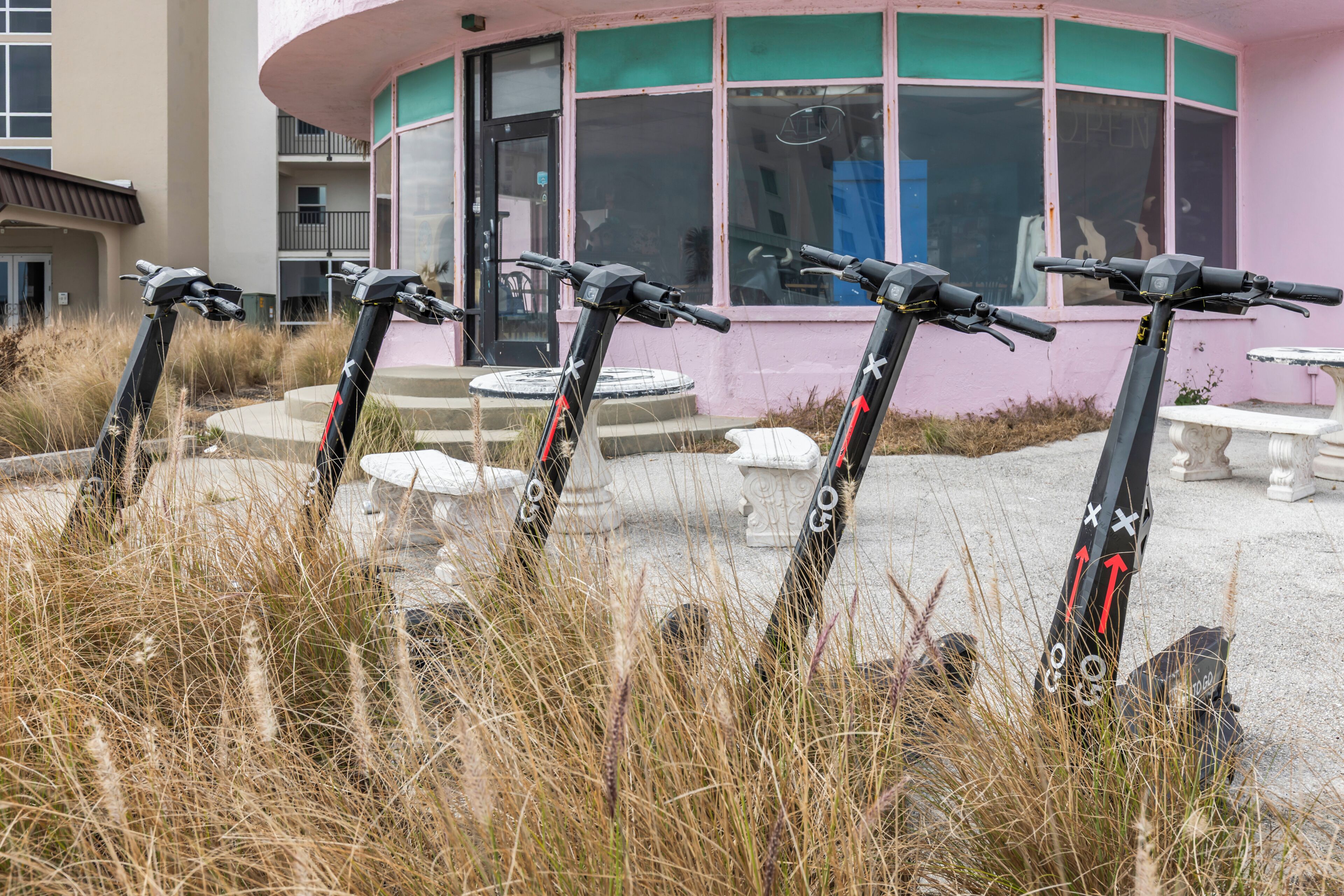 Four scooters parked in front of a building with a pink exterior and large windows.