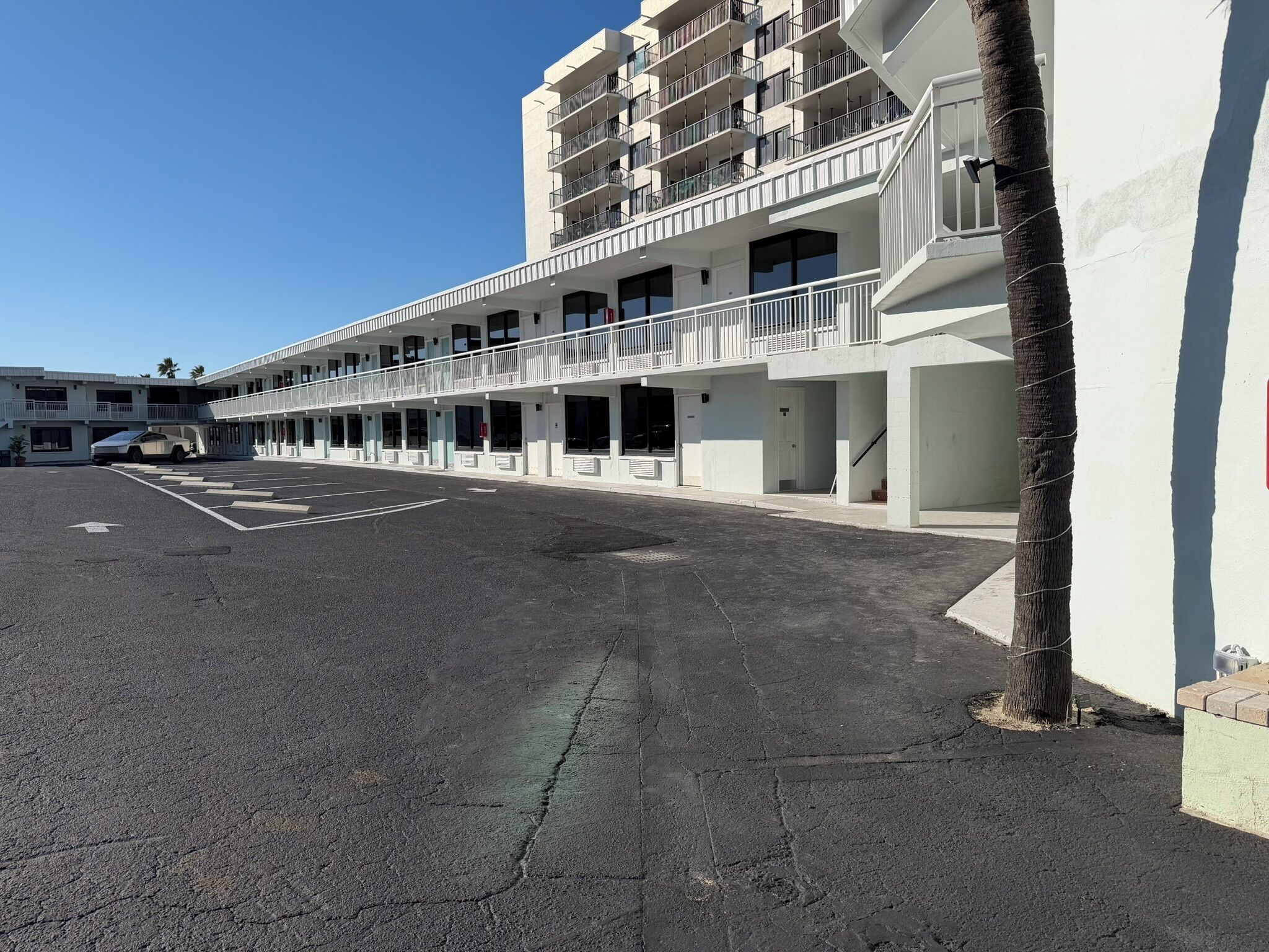 A multi-story hotel with balconies, a parking lot, and a clear sky.