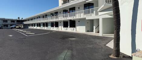 A multi-story hotel with balconies, a parking lot, and a clear sky.