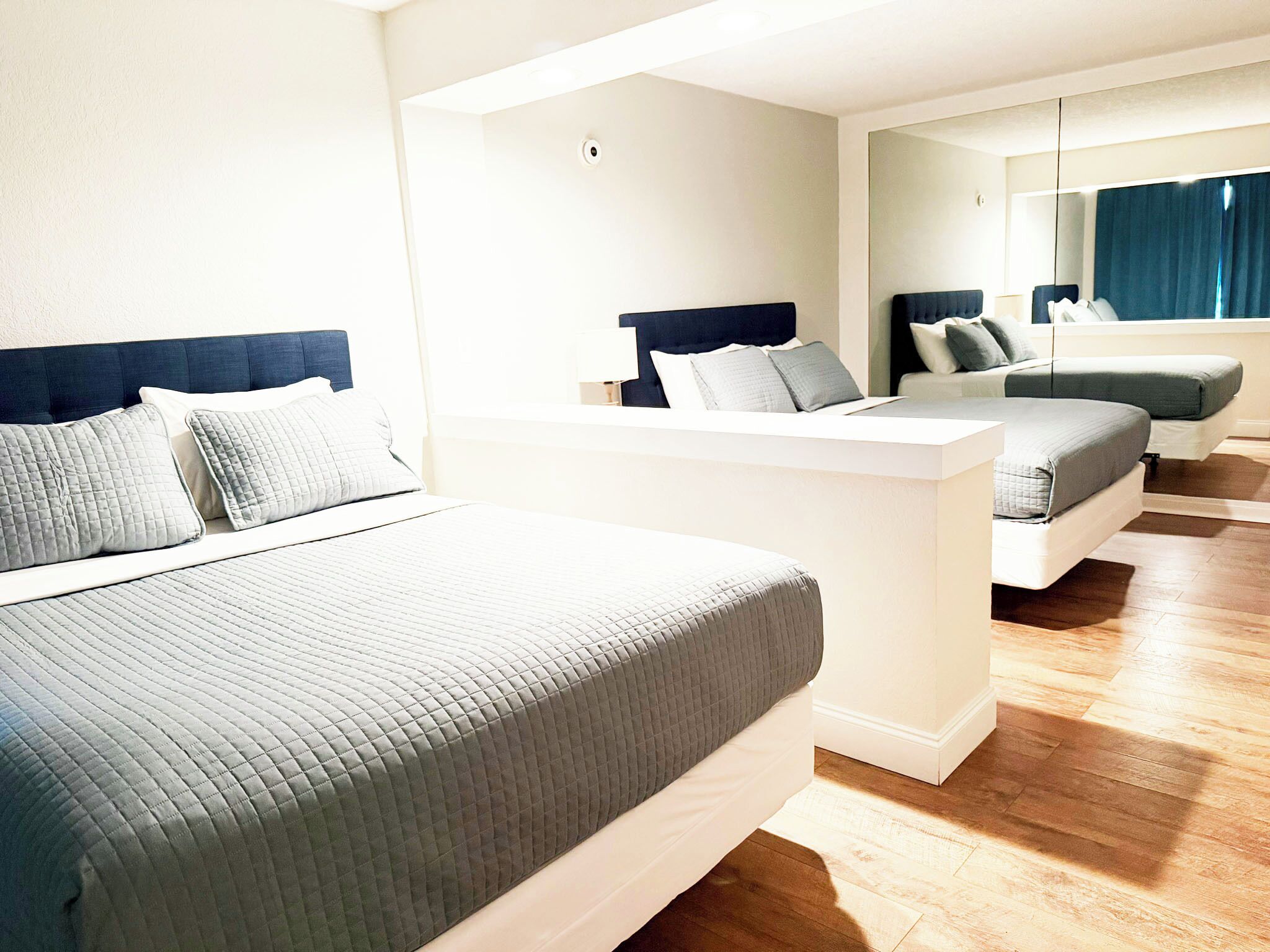 A hotel room with a large bed, a smaller bed, a desk, and a mirror.