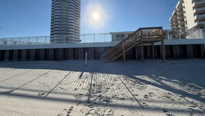 Ein Strand mit einer Holzpromenade, die zu einem Gebäude mit mehreren Balkonen führt.
