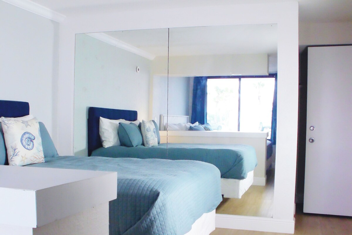 Ein Schlafzimmer mit zwei Betten, einem großen Spiegel und Blick auf einen Balkon.