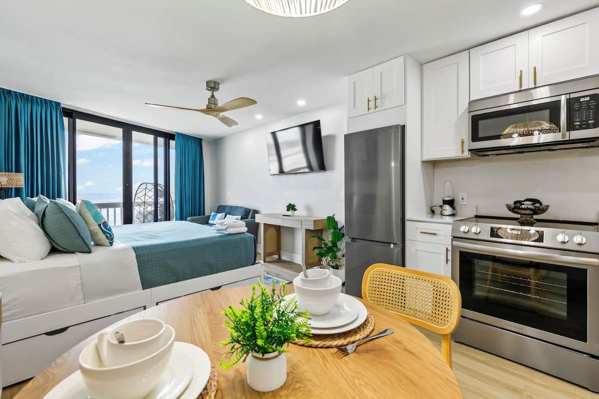 A modern kitchen with a flat-screen TV, stainless steel appliances, and a dining area with a wooden table and chairs.