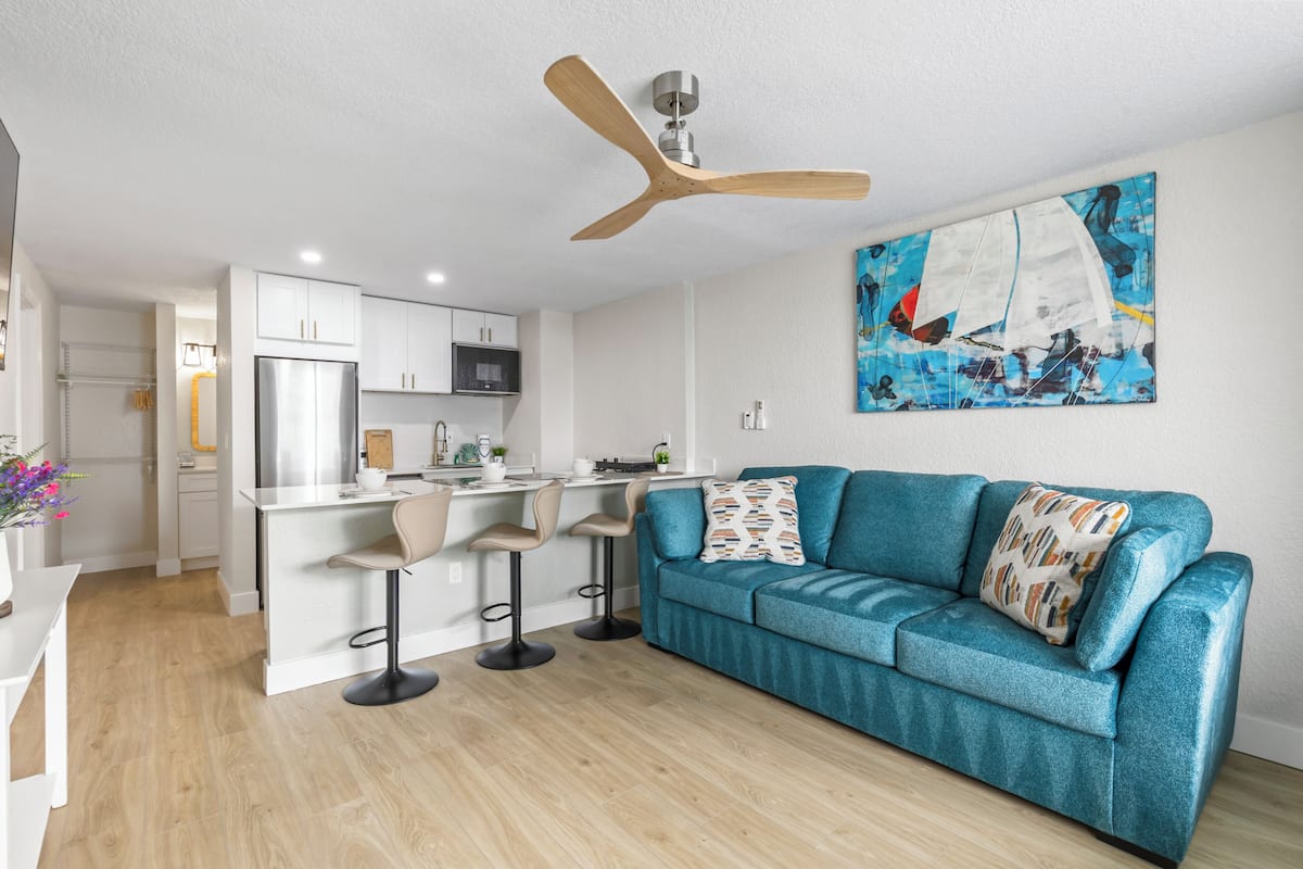 A modern kitchen with white cabinets, a stainless steel refrigerator, and a bar area with stools.