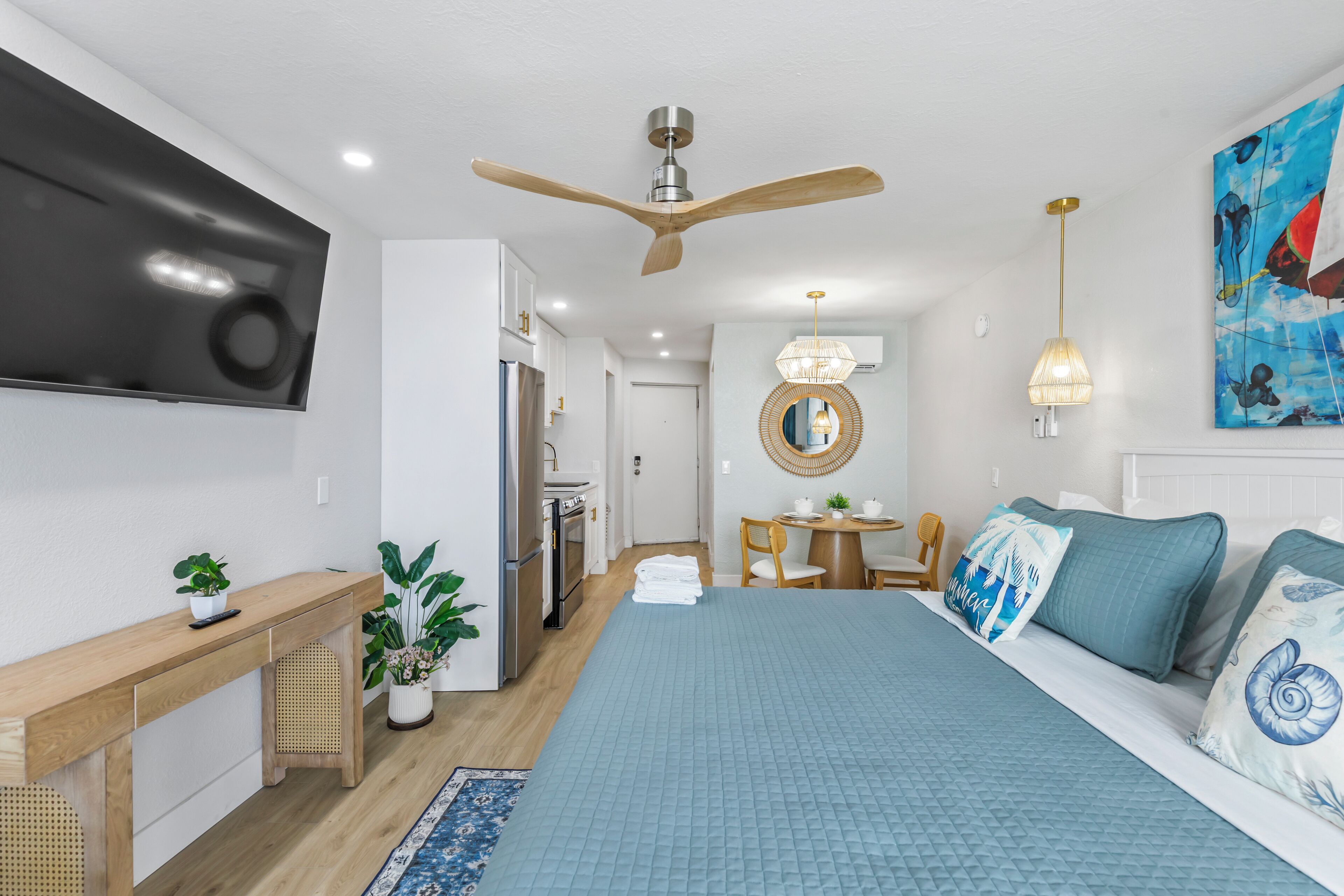 Un dormitorio moderno con una cama grande, ventilador de techo, televisión de pantalla plana, zona de comedor y cocina.