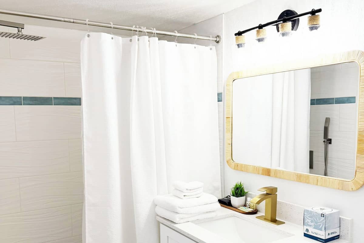 A bathroom with a shower, a sink with a gold faucet, a mirror with a gold frame, and a toilet paper holder.