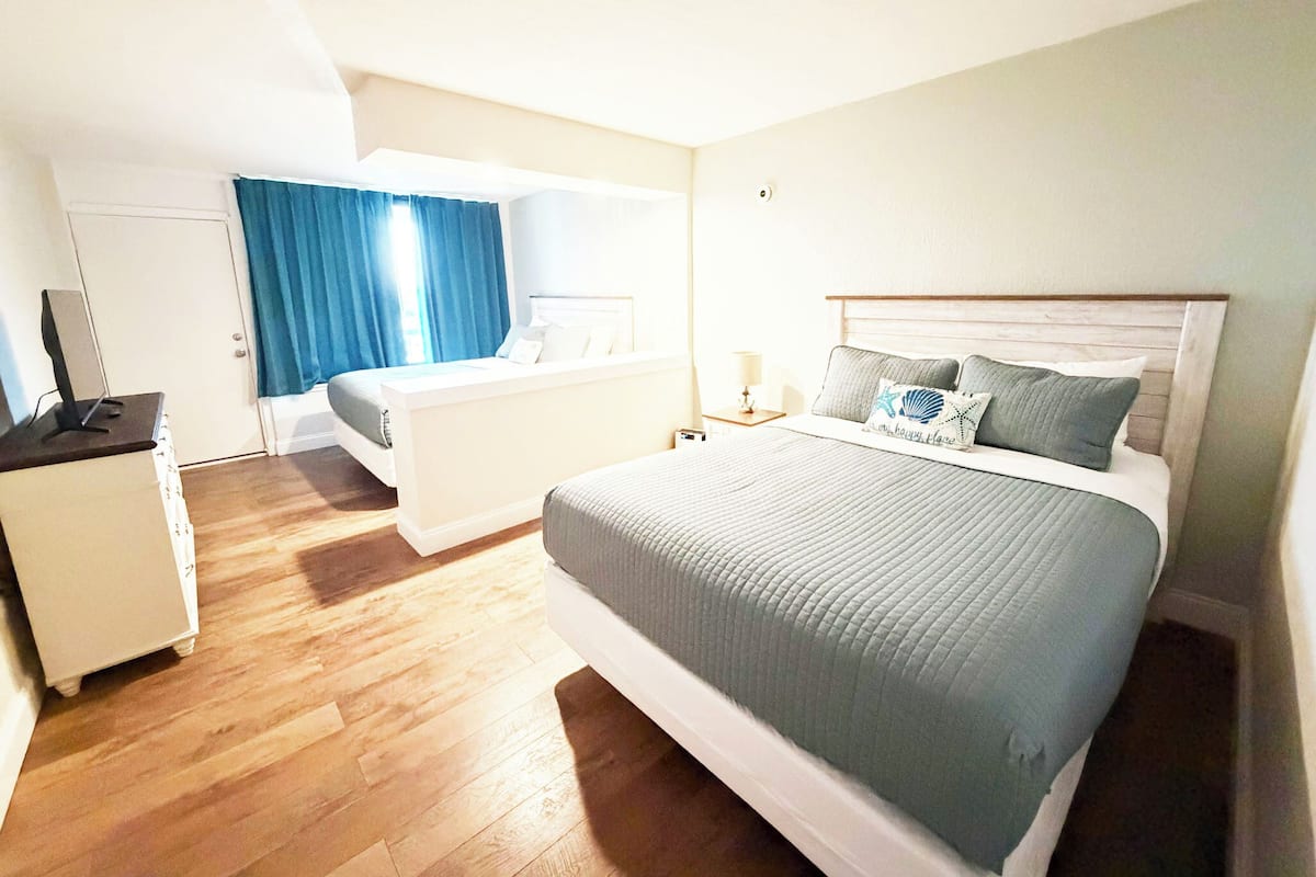 A hotel room with a bed, a desk, a chair, a window with curtains, and a door.