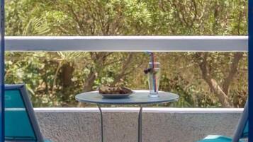 Un balcón con dos sillas turquesas, una mesita redonda con comida y una bebida, y vistas a vegetación exuberante.