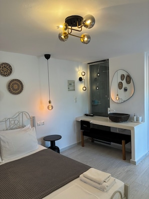 A modern bedroom with a bed, bedside table, and a desk with a mirror. - Anamnisi Studio (Milos)