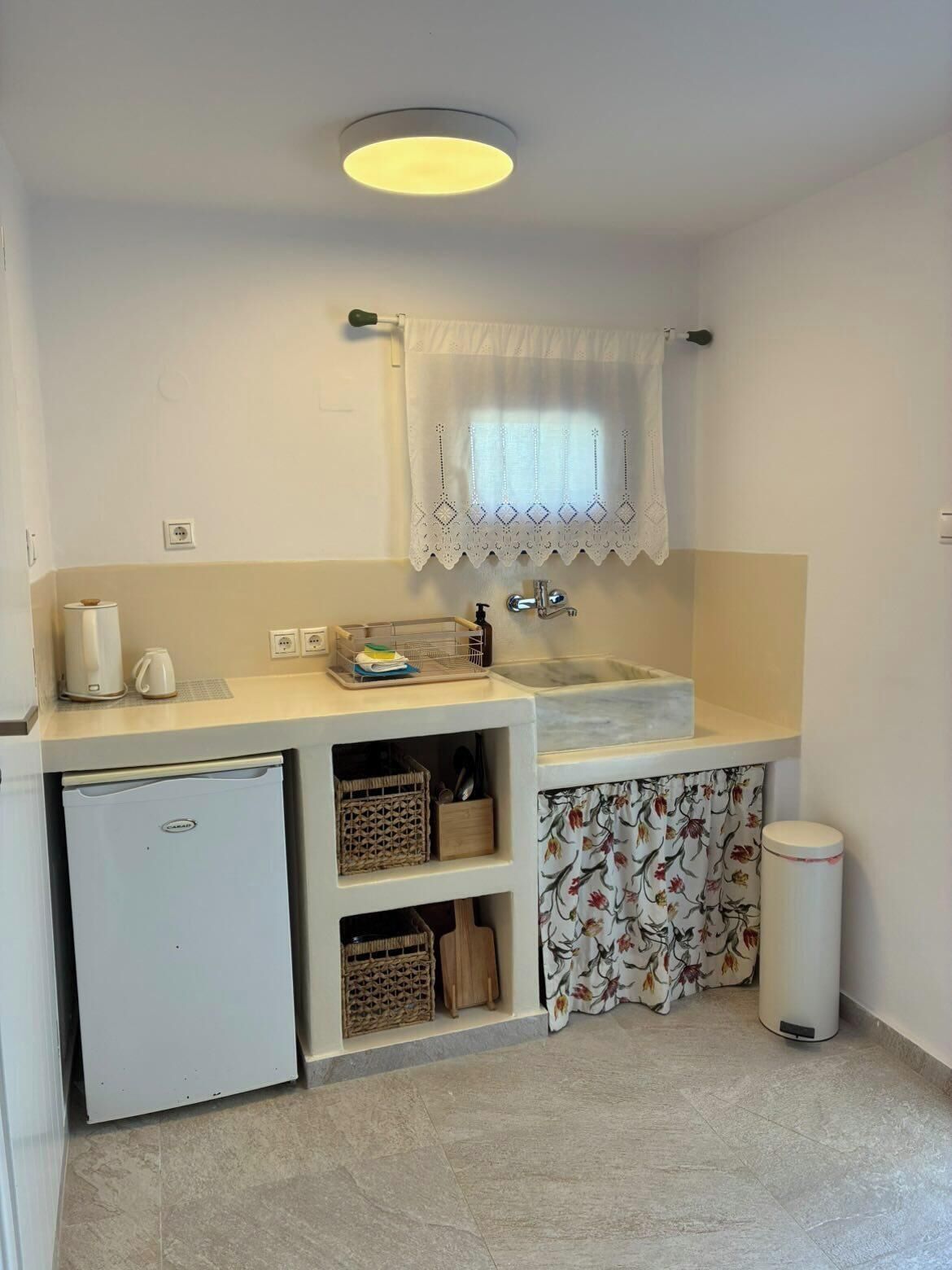 Una cocina compacta con un lavamanos, un refrigerador pequeño y estantes para guardar objetos.