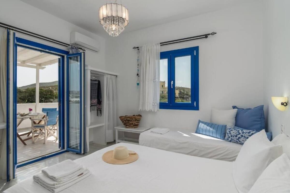Une chambre à coucher avec un lit, une fenêtre avec des volets bleus, un lustre et une vue sur l’extérieur.