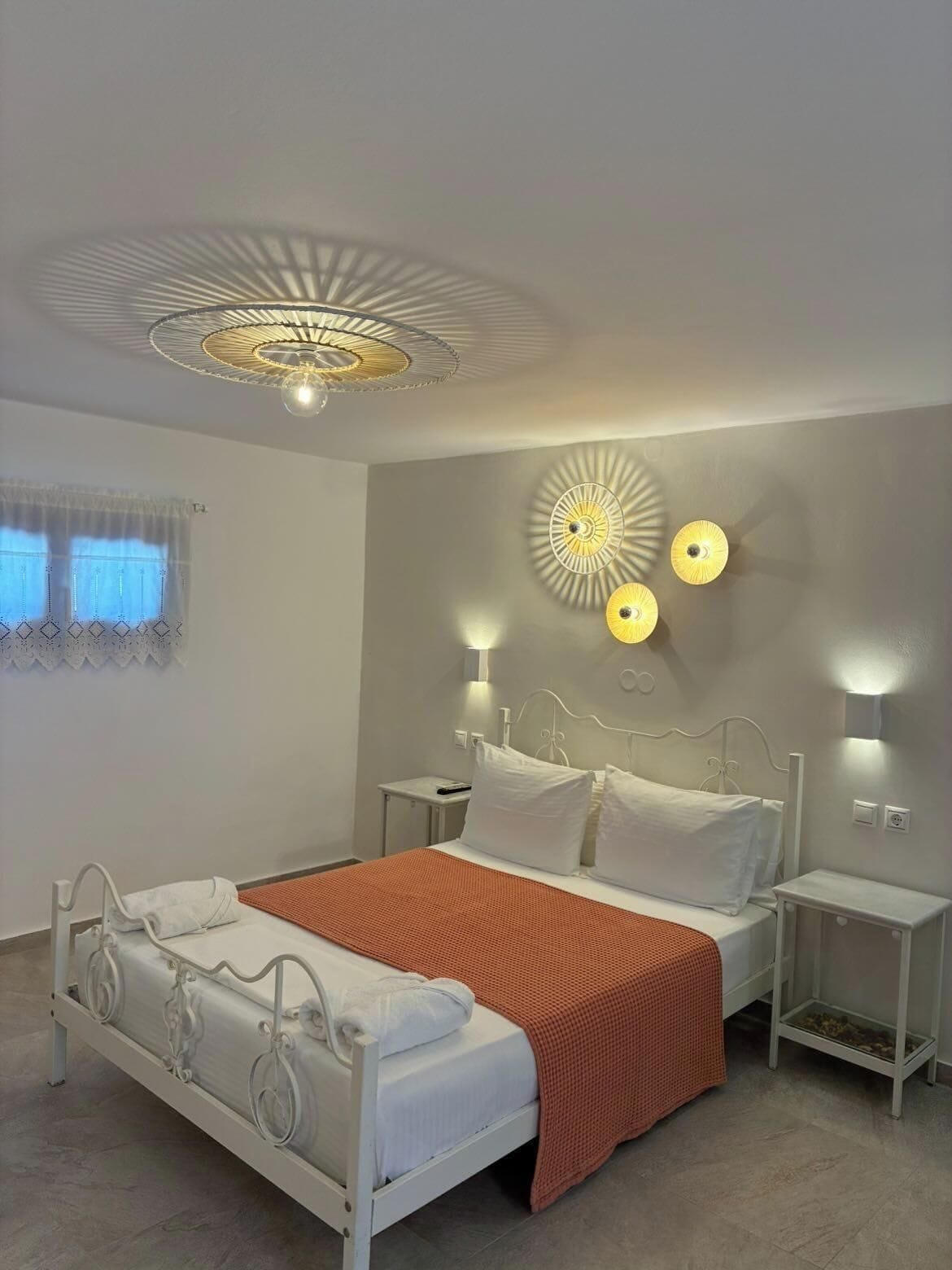 A modern bedroom with a bed, bedside tables, a ceiling light fixture, and wall-mounted lamps.