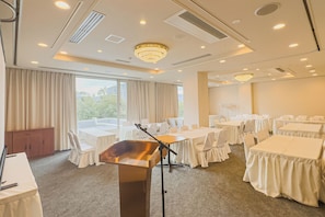 A conference room with multiple tables and chairs, a podium, and large windows with curtains.