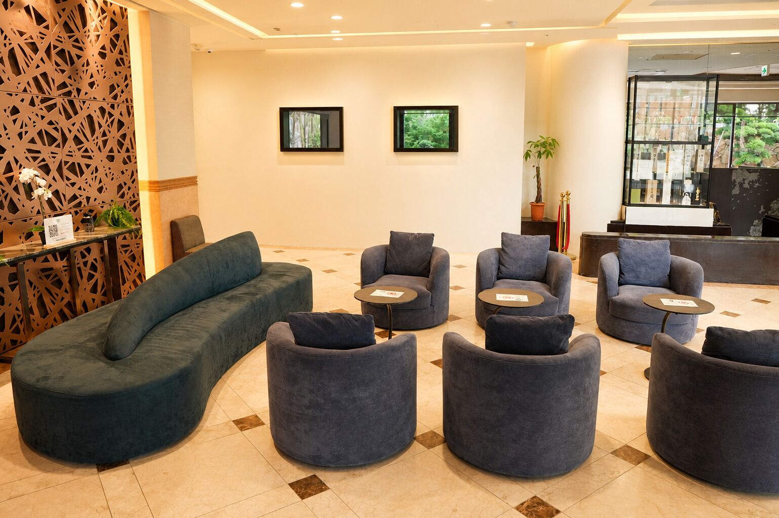 Ein stilvoller Lounge-Bereich mit gebogenem Sofa, mehreren Sesseln und runden Tischen, ausgestattet mit einer Wanddekoration und einer Rezeption.