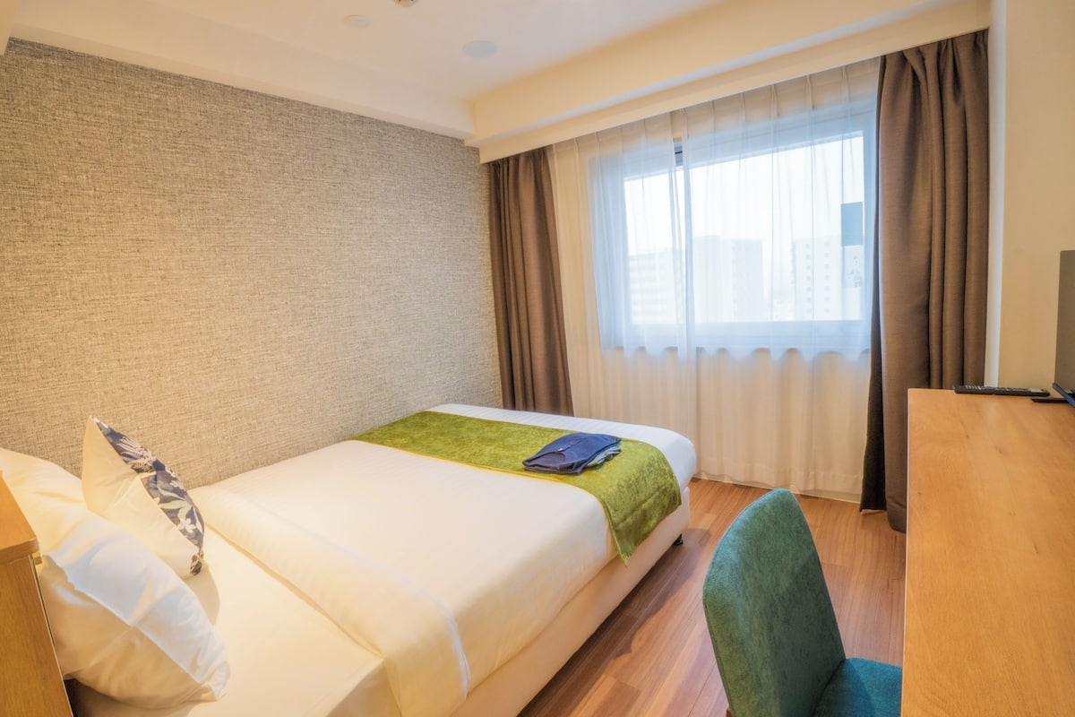 A hotel room with a bed, a desk, and a chair.
