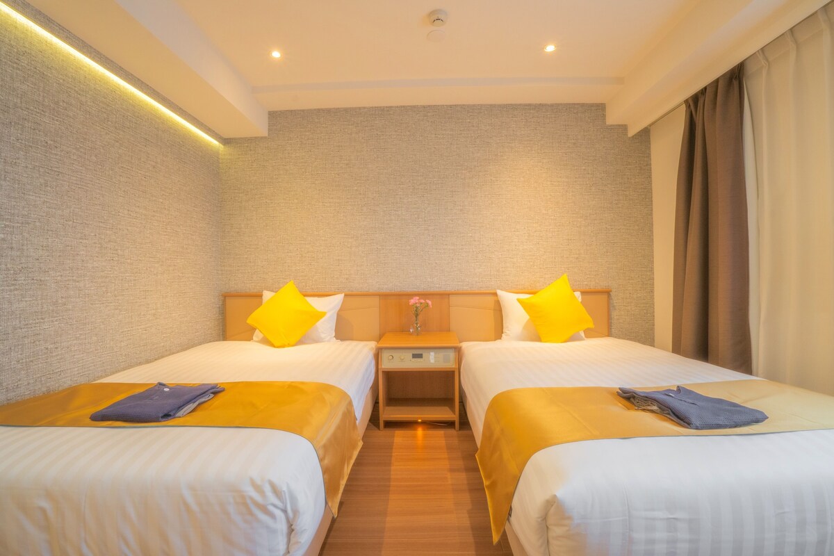 Ein Hotelzimmer mit zwei Betten, einem Nachttisch und einem an der Wand befestigten Regal.
