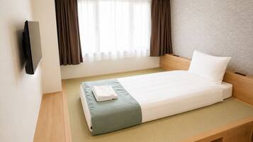 A hotel room with a bed, a TV mounted on the wall, and a window with curtains.