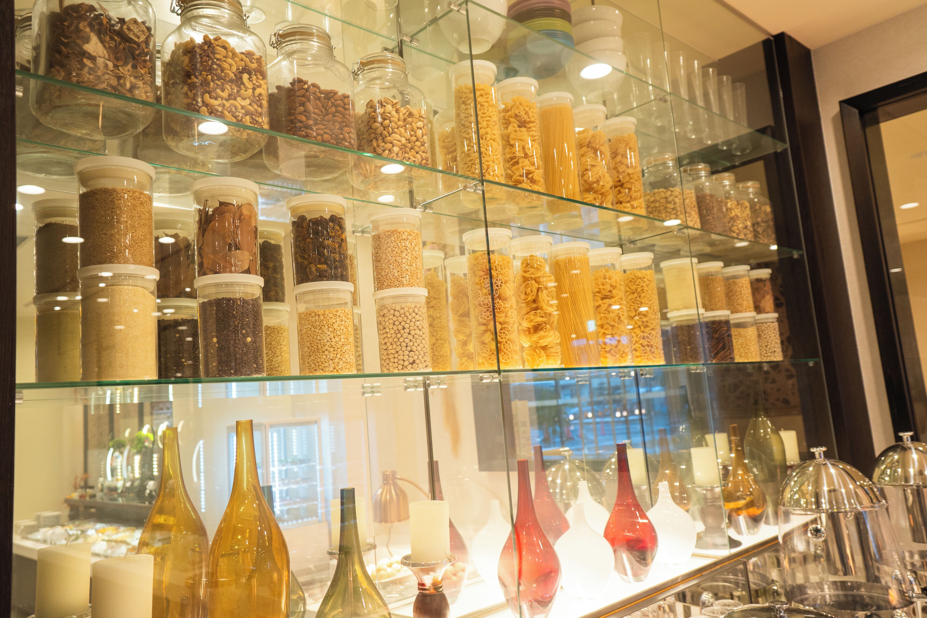 A display of glass jars containing various nuts and grains, and several glass vases on shelves.