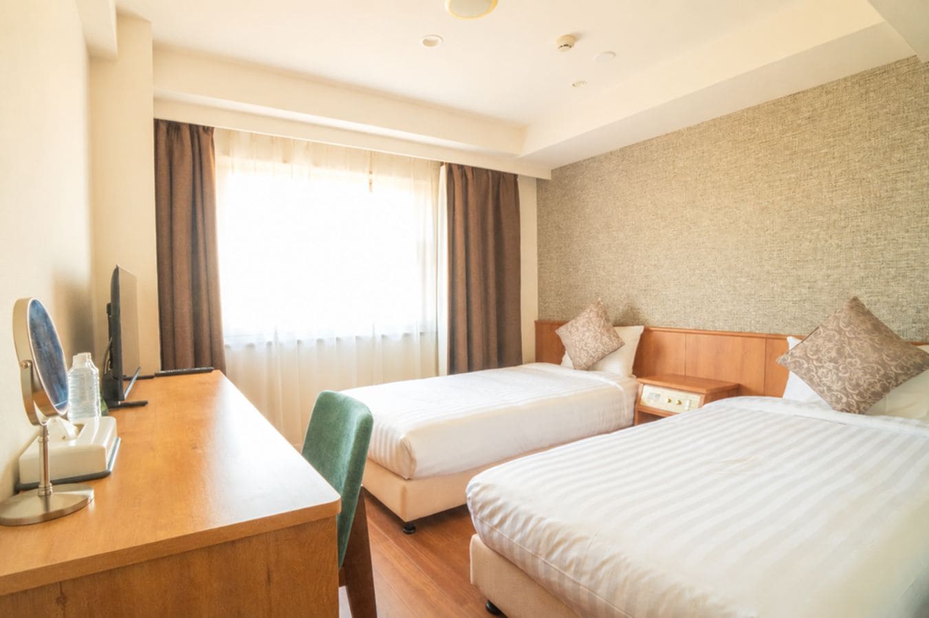 Habitación de hotel con dos camas, un escritorio con un espejo y una botella, y un televisor.