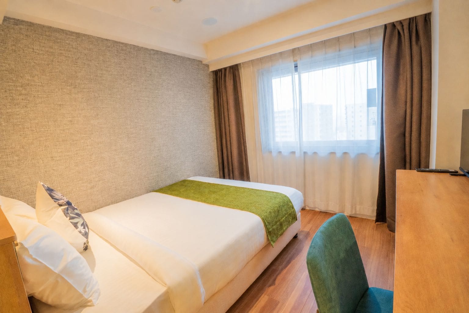 A hotel room with a bed, a desk, a chair, and a window with curtains.