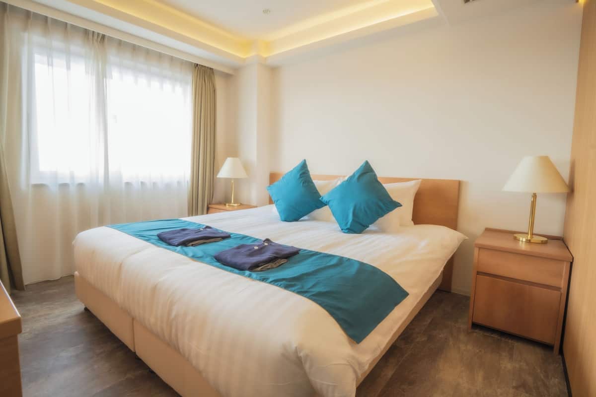 Una cama bien hecha con ropa de cama azul y blanca, dos lámparas de noche y una mesita de noche de madera.