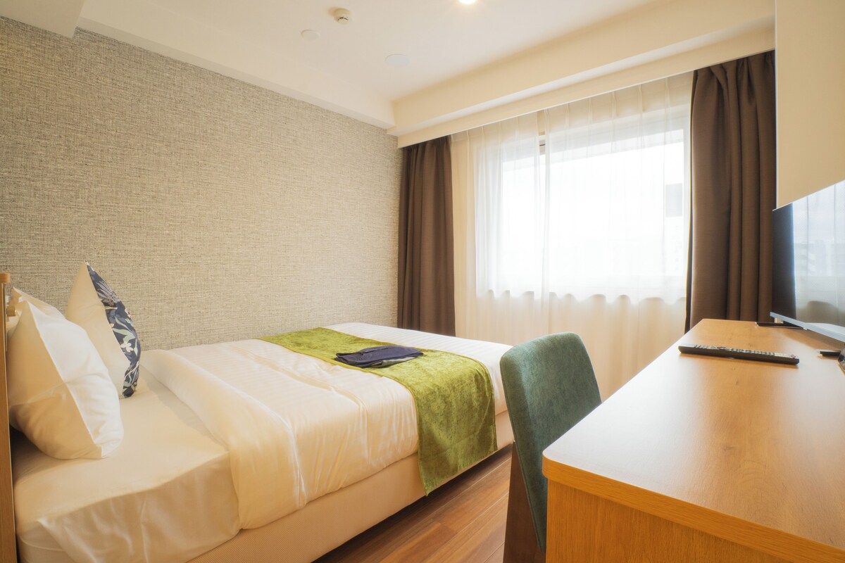 Ein Hotelzimmer mit Bett, Schreibtisch, Fernseher und einem Fenster mit Vorhängen.