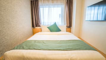 A hotel room with a bed, a nightstand, a window with curtains, and a wall with a textured pattern.