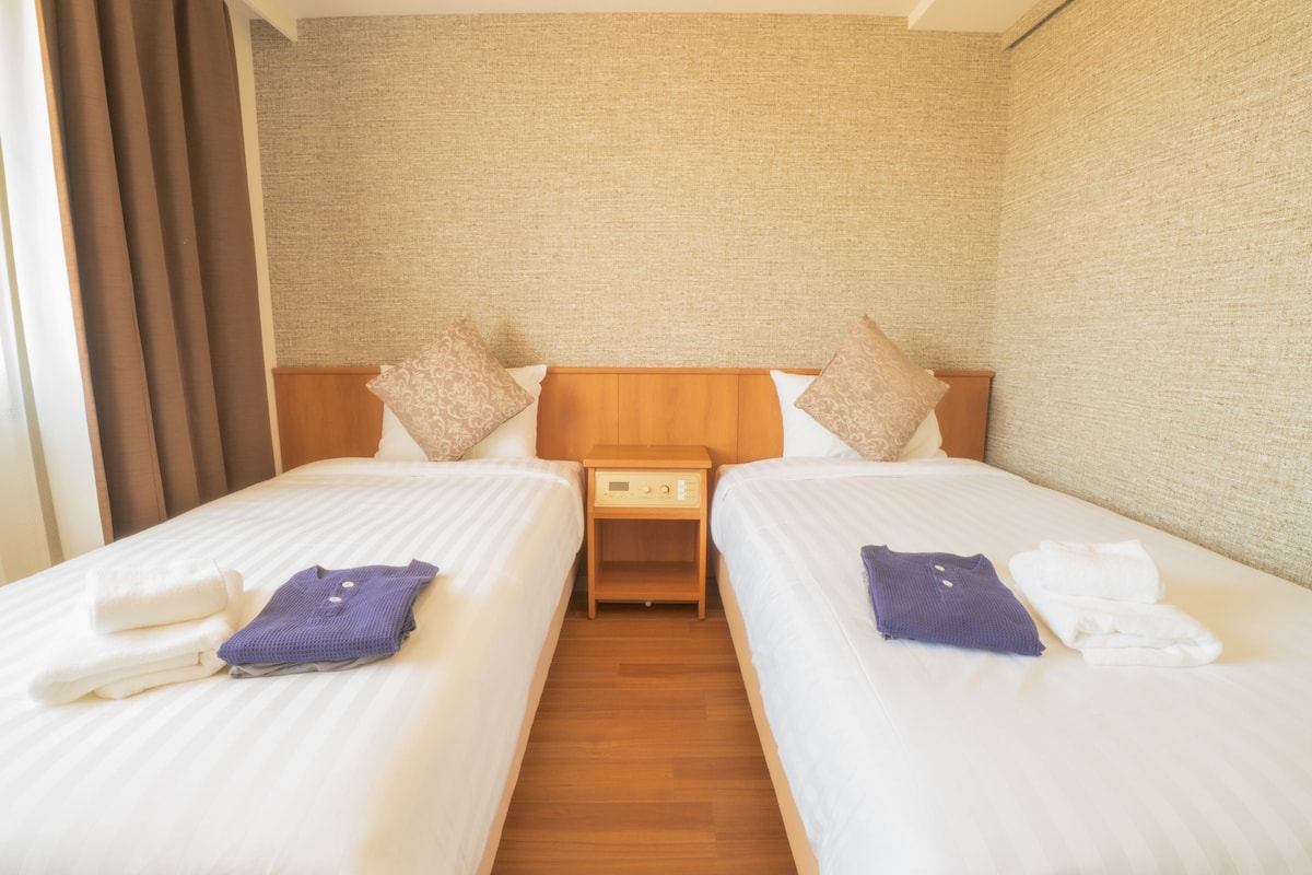 A hotel room with two single beds, a wooden nightstand, and a headboard with a textured wall behind.