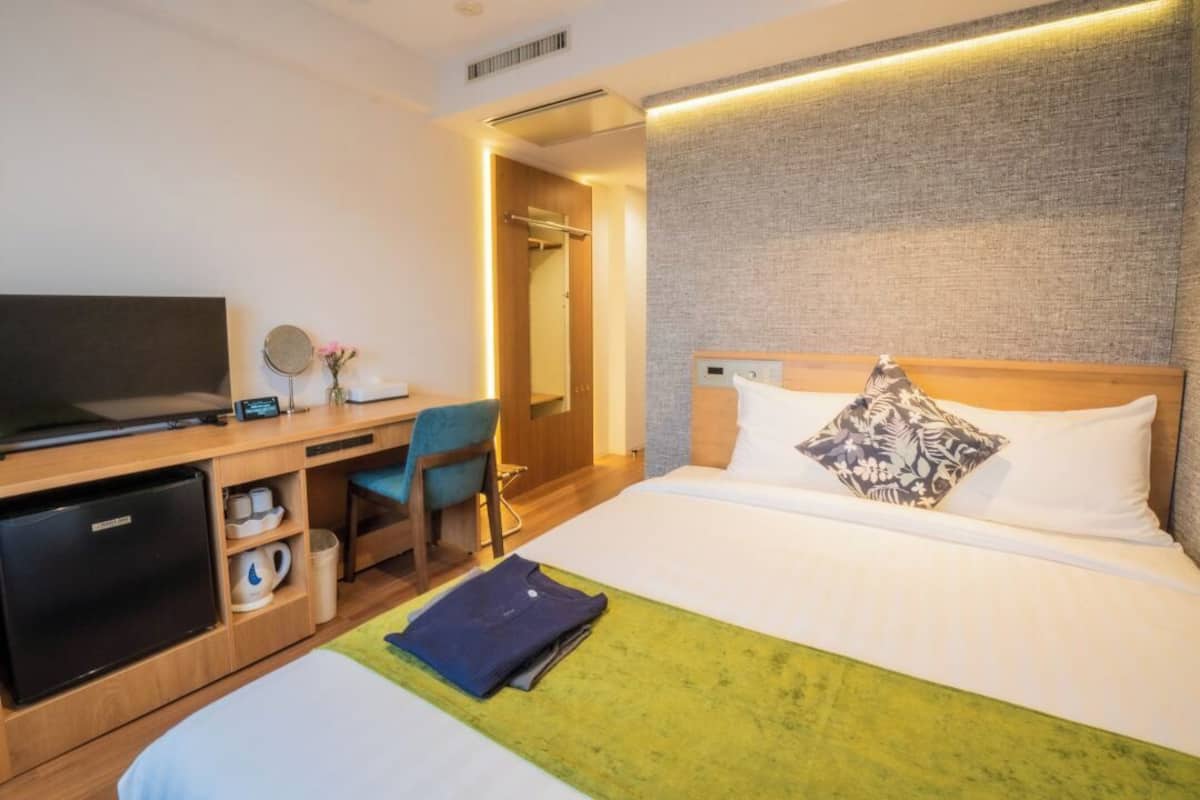 Una habitación de hotel con cama, escritorio, computadora, y un refrigerador pequeño.