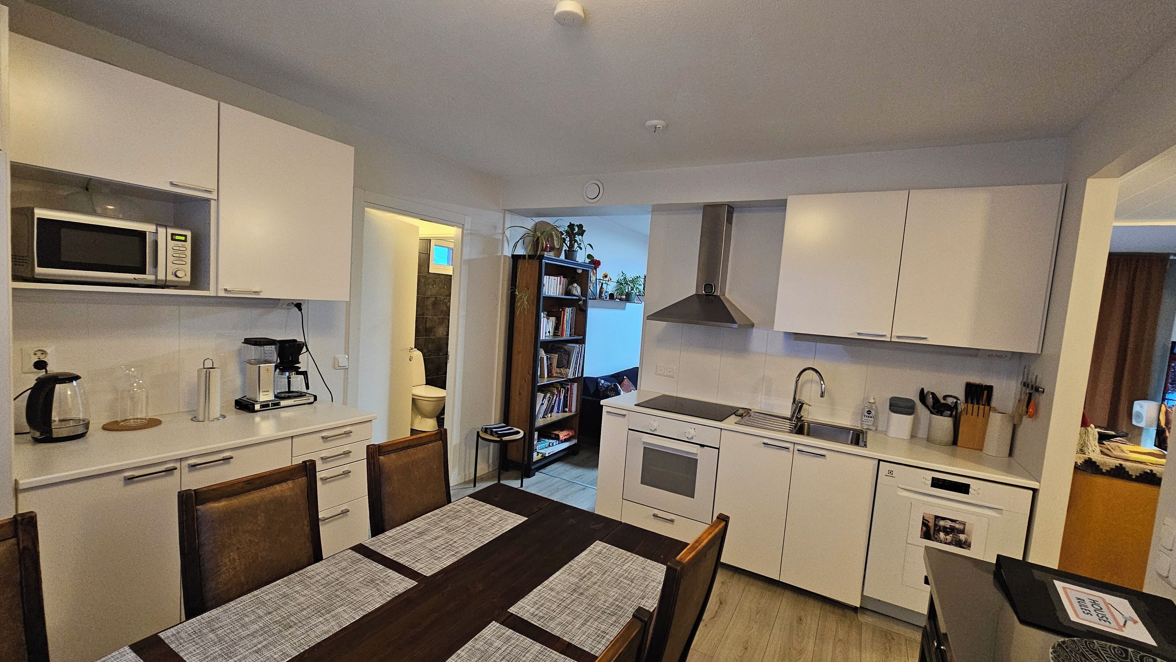 A compact kitchen with white cabinetry, a microwave, a coffee maker, and a dining area with a table and chairs.