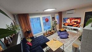 A living room with a dark blue sofa, a wooden coffee table, and a large flat-screen TV displaying a cozy interior scene. - Cozy home with sauna and kota (Rovaniemi)