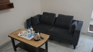 A living room with a dark grey sofa, a wooden coffee table with a tray of items including bottles and a kettle, and a marble-tiled floor. - S L N COMFORT (Bengaluru)