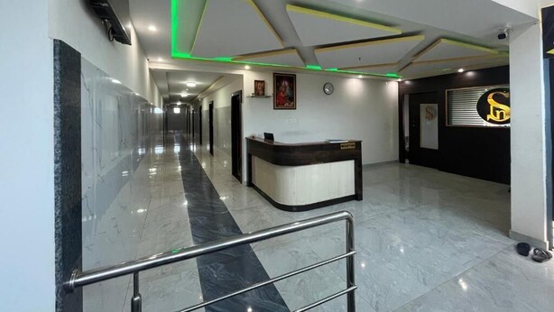 A modern hotel lobby with a reception desk, a marble floor, and a ceiling with geometric patterns and green lighting accents. - S L N COMFORT (Bengaluru)