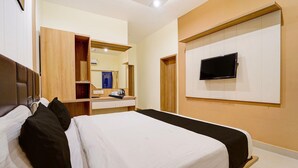 A hotel room with a bed, a TV mounted on the wall, a wooden wardrobe, and a mirror. - Townhouse Dindigul Rock Fort Formerly Ramora Grand (Thindukkal)