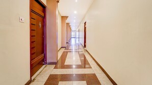 A long, narrow hallway with wooden doors and a checkered floor. - Townhouse Dindigul Rock Fort Formerly Ramora Grand (Thindukkal)