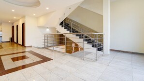 A spacious interior with a modern staircase, a central open area, and a hallway leading to doors. - Townhouse Dindigul Rock Fort Formerly Ramora Grand (Thindukkal)
