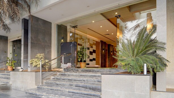 A modern hotel entrance with a marble staircase, potted plants, and a glass door leading inside. - Townhouse Dindigul Rock Fort Formerly Ramora Grand (Thindukkal)