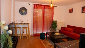 Ein Wohnzimmer mit einem roten Sofa, einem Couchtisch, einem Esstisch mit Stühlen, einer Uhr und einer Pflanze.