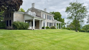 A large, two-story house with a stone facade, a covered porch, and a well-maintained lawn. - Private Beach with Views: Stonehouse Estate, Near Wine Trail and Spa (Aurora)