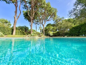 A clear swimming pool surrounded by lush greenery and tall trees. - VILAMOURA AMAZING VILLA 2 WITH POOL by HOMING (Vilamoura)