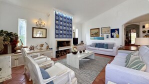 Un salon spacieux avec une cheminée, des meubles blancs et un mur orné d’un motif bleu.