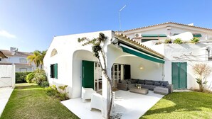Une maison moderne avec une façade blanche, des volets verts et un espace extérieur aménagé avec un canapé et une table basse.