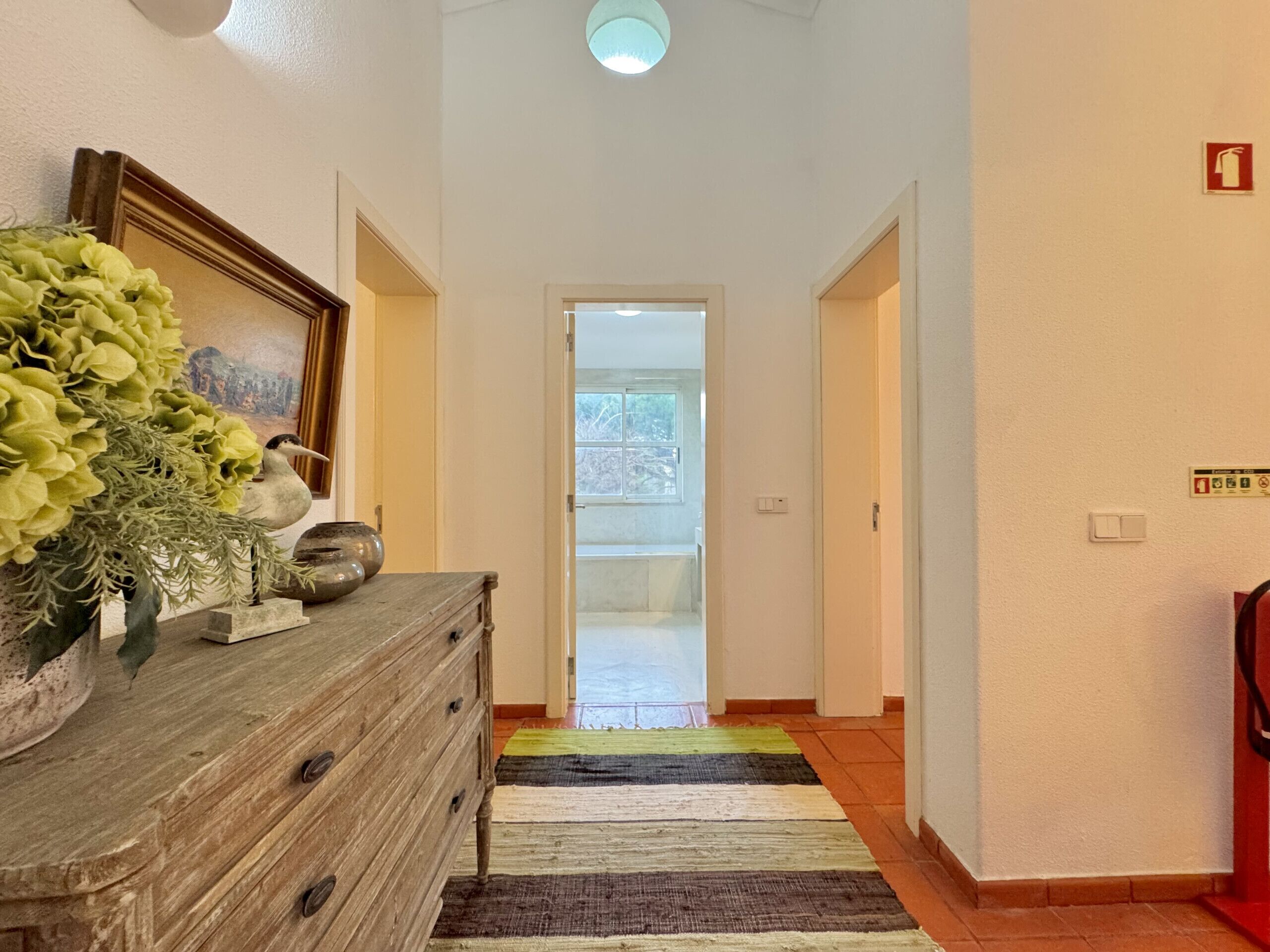 A hallway with a wooden dresser, a framed picture, and a vase of flowers.