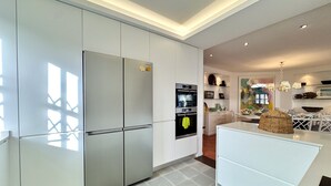 Une cuisine moderne avec des meubles blancs, un four encastré et un coin repas comprenant une table et des chaises blanches.